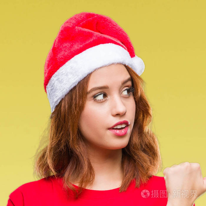 年轻美丽的女人在孤立的背景下穿着圣诞帽微笑着快乐的脸看着, 并指向侧面与拇指向上