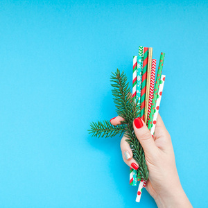 新年圣诞佳节庆典女子手红色修指甲饮鸡尾酒派对吸管复制空间绿松石蓝彩纸背景最小风格。方形模板贺卡