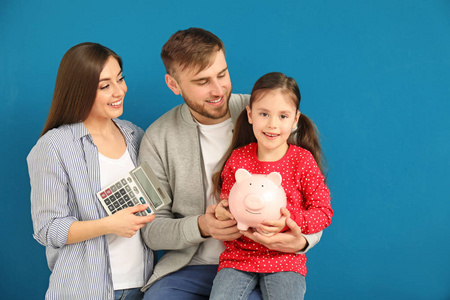 快乐的年轻家庭与小猪银行和计算器在颜色背景