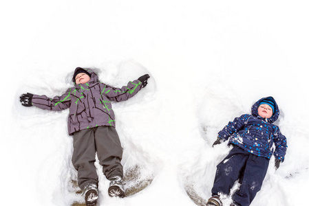 两个小姐妹孩子男孩在多彩冬季服装制作雪天使，躺在雪中。与孩子在冬天的户外活动休闲。快乐的兄弟