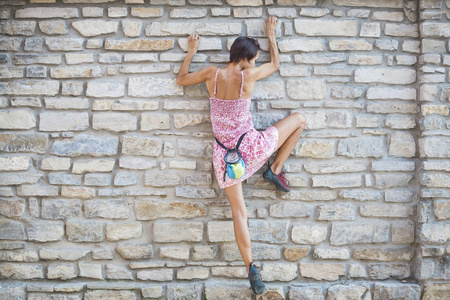 女孩爬上了石墙。一个穿着夏装的女人爬上了一座旧房子的墙。砖栅栏。登山者正挂在城市建筑上。加强毁坏的城堡