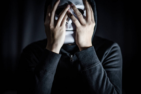 神秘的帽衫人穿着白色面具在黑暗的房间。匿名社交屏蔽。主要抑郁症或躁郁症。万圣节概念