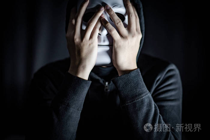 神秘的帽衫人穿着白色面具在黑暗的房间.匿名社交屏蔽.