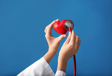 医用听诊器和红色心脏的心脏病专家的手在颜色背景