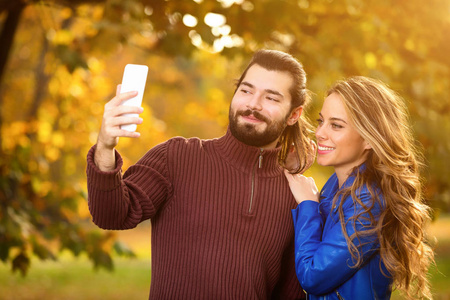 可爱的夫妇使用手机在公园秋季秋季颜色