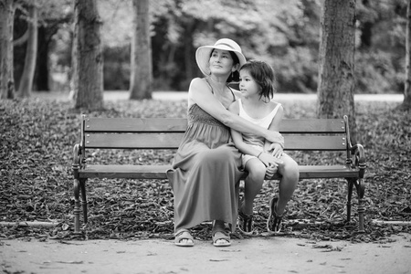 秋季公园坐长椅上的成年女子拥抱小女孩