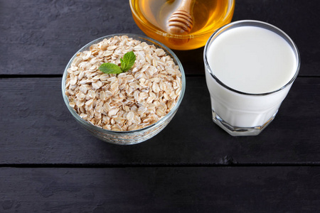 燕麦片, 玻璃牛奶和蜂蜜用木棍.在黑色木板上早餐的燕麦粥.健康食品.