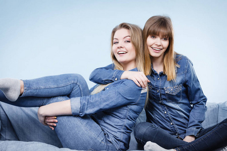 友谊，人类关系概念。两个快乐的女性朋友或姐妹穿牛仔裤衬衫坐在沙发上开心的谈话