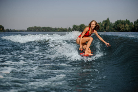 快乐和微笑的金发女郎 wakesurfer 在温暖的一天骑下蓝色飞溅的波浪