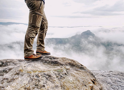 长疲倦的男性腿在徒步旅行长裤停留在岩石山顶的片刻在谷之上
