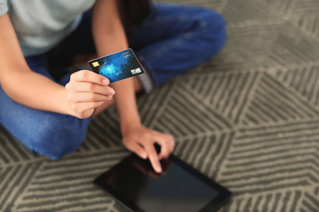 年轻妇女在网上购物与信用卡和平板电脑在家里