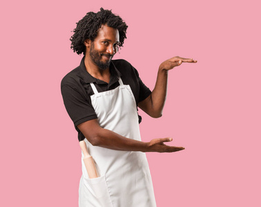 手拿着对象英俊的非洲裔美国人面包手拿着东西, 展示一个产品, 微笑和