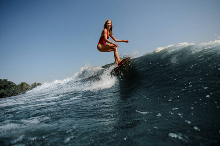 高蓝色波浪在前景和美丽的金发妇女 wakesurfing 在船上在背景上