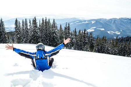 年轻英俊的男子在冬季运动服看着, 戴着大镜子滑雪面具. 穿着蓝色滑雪服的男子坐在山顶上的雪上。