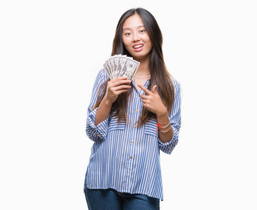 年轻的亚洲妇女持有美元在孤立的背景非常高兴地指着手和手指