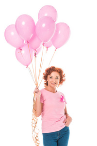 快乐成熟的女人抱着一堆粉红色的气球, 微笑着在白色的相机隔离, 乳腺癌的概念