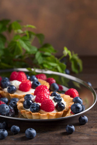 在木桌上放有覆盆子和蓝莓的甜点馅饼。特写的花哨的美食新鲜浆果甜点挞
