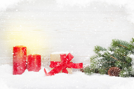 圣诞礼品盒, 蜡烛和冷杉树枝覆盖在木墙前的雪。使用复制空间查看