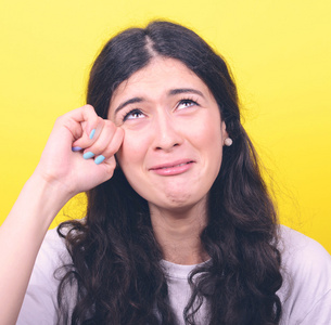 女人哭,擦干眼泪对黄色背景的肖像照片