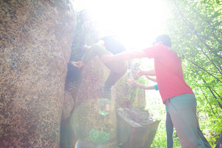 在自然里爬山。朋友爬到那块石头。这个女孩爬上石头，和朋友支持她。在自然的抱石。积极的生活方式。运动的人。体操保险