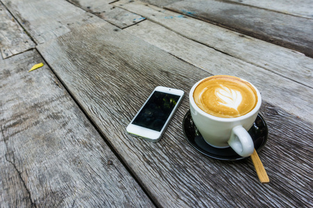拿铁咖啡杯子和手机业务在木桌上，选择性地专注于咖啡