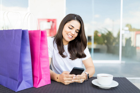 美丽的女性购物者在咖啡桌上的智能手机上发短信