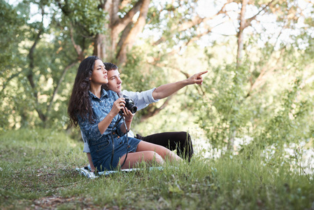 年轻夫妇坐在草地上的森林, 拍照和看日落, 夏季自然, 明亮的阳光, 阴影和绿叶, 浪漫的感觉