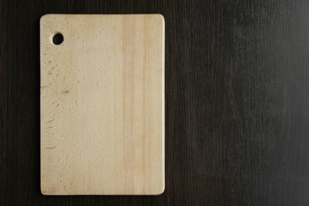 浅黄色木制切割板位于深褐色的木桌背景上
