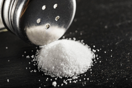 细磨的盐从盐瓶上散落在黑色的桌子上。地方为 tex