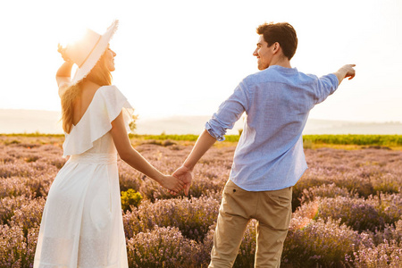 快乐的年轻夫妇拥抱在薰衣草领域, 指着手指