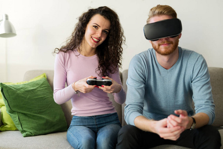 幸福小两口玩视频游戏与虚拟现实的耳机在家里