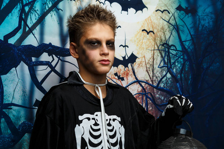 可爱的, 年轻的男孩穿着骷髅服装, 站在前面的背景与蝙蝠和黑暗森林.