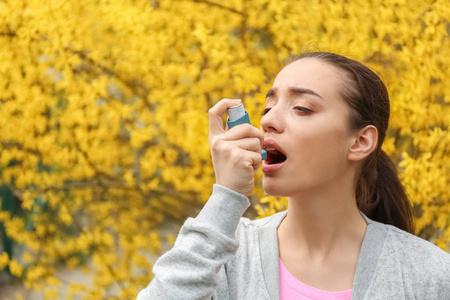 年轻妇女使用吸入器附近开花树。过敏概念