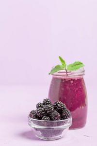 黑莓奶昔生有机饮料与新鲜成熟的森林浆果在柔和的紫罗兰色背景。素食甜维他命生态饮料健康饮食理念