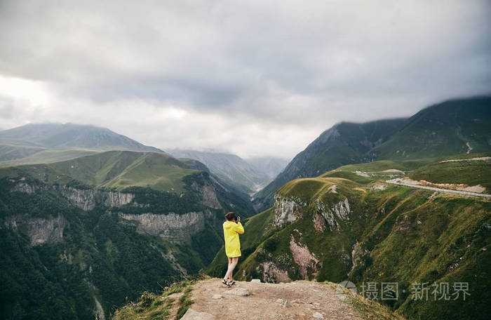 照片 人物 一个穿着黄色雨衣的年轻女孩在山上拍照.格鲁吉亚.夏天.