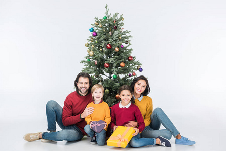幸福的家庭坐在圣诞树旁边的礼物被孤立的白色