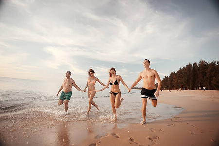 四朋友在海滩上跑步, 暑假和幸福的概念。在海岸边乐趣的年轻男子和妇女