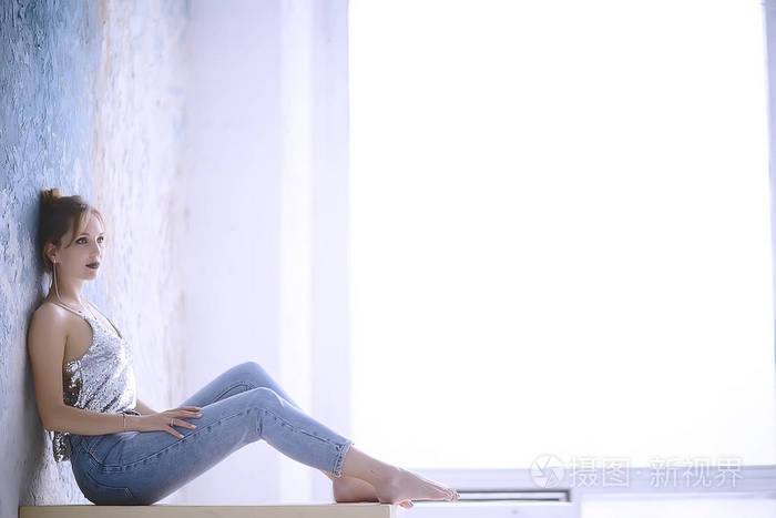 有吸引力的年轻女子穿着苗条的牛仔裤摆在靠墙