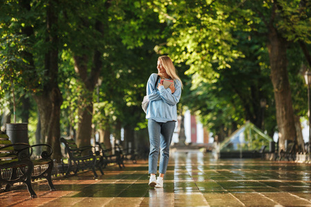 微笑的年轻女孩与书包背着书, 在公园散步照片