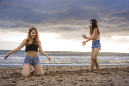 两位快乐迷人的亚洲华人女性女友或姐妹玩沙滩上的沙子在美丽的阳光下享受夏日假期一起无忧无虑的旅行