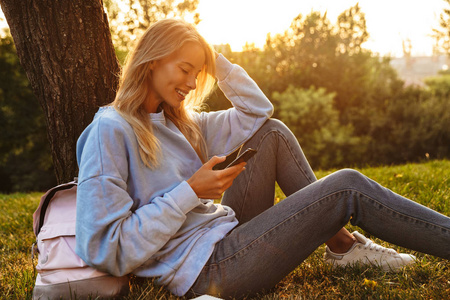 一个快乐的年轻女孩的肖像坐在草地上的公园, 使用手机