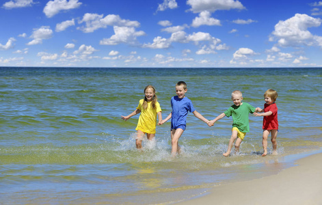 两个女孩和两个男孩在五颜六色的 t恤衫上奔跑在沙滩上, 蓝天白云在后台