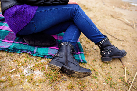 穿着蓝色牛仔裤和黑色冬季靴子的女子脚在沙滩上