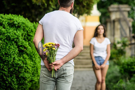 第一印象总是重要的。男人在等待女孩浪漫的约会时藏在后面的花花束。给她一个惊喜。约会公园背景的情侣会议。男友为女友准备了惊喜