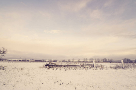 冬季景观中的木栅栏在早晨的田野上下雪