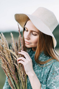 美丽的俄罗斯女孩在帽子和夏季礼服, 走在田野上的草地上的腰部。快乐的旅行者, 收集草药, 微笑。森林中的日落
