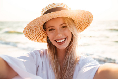 正面金发女人的肖像20s 在夏天草帽微笑着, 并采取自拍, 而在海滨散步
