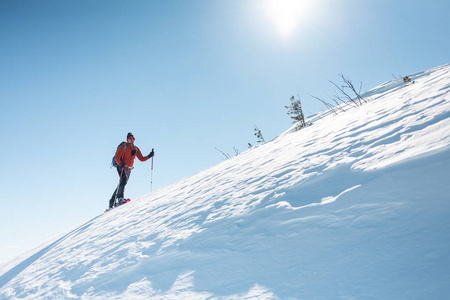 一个人爬上山顶。登山运动员在雪地鞋背着一个背包。在冬天的山上旅行。大自然中的极端假期。极端条件下的旅游者