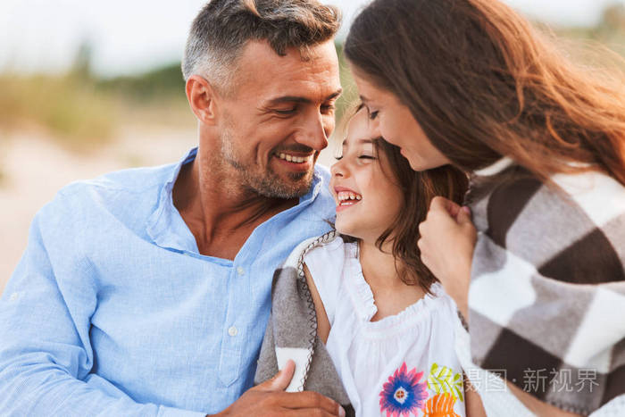 年轻可爱的父母拥抱在海滩与他们的女儿在户外的形象