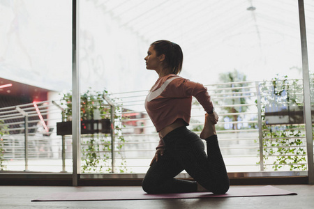 漂亮的微笑女人坐在一条腿上的王鸽运动, eka pada rajakapotasana 的姿势。美丽的女孩在室内做瑜伽。在体育中